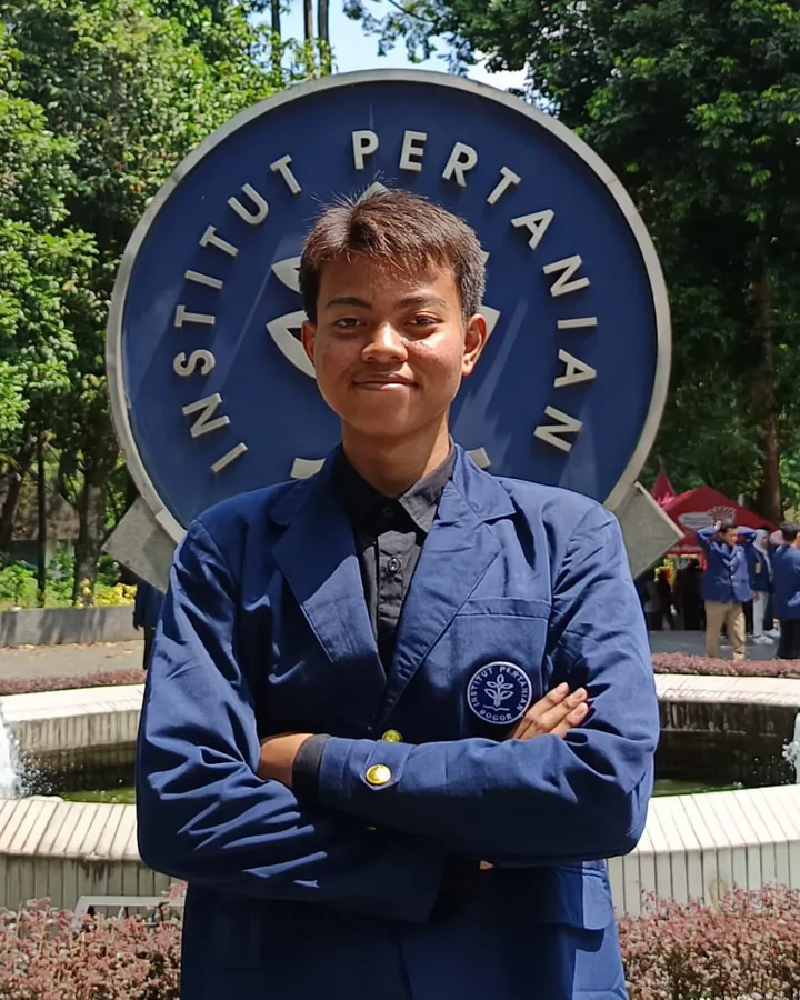 Aditya Cahyo Nugroho wearing a blue IPB campus uniform in front of the university monument